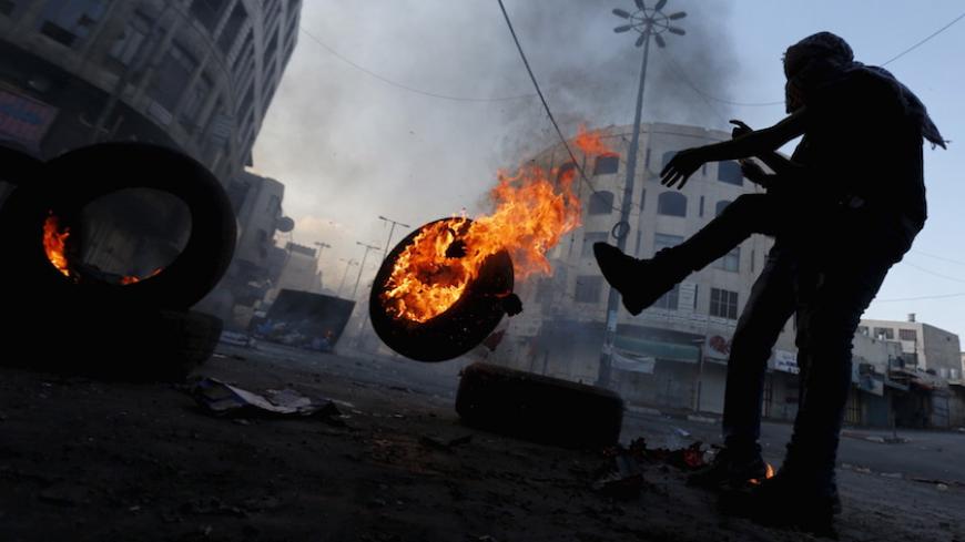 A Palestinian protester pushes a burning tyre during clashes with Israeli troops in the West Bank city of Hebron October 31, 2015. Israeli security forces shot and killed a Palestinian who ran at them with a knife in the occupied West Bank on Saturday, police said, as a month-long wave of violence showed no signs of abating. REUTERS/Ammar Awad - RTX1U4BU