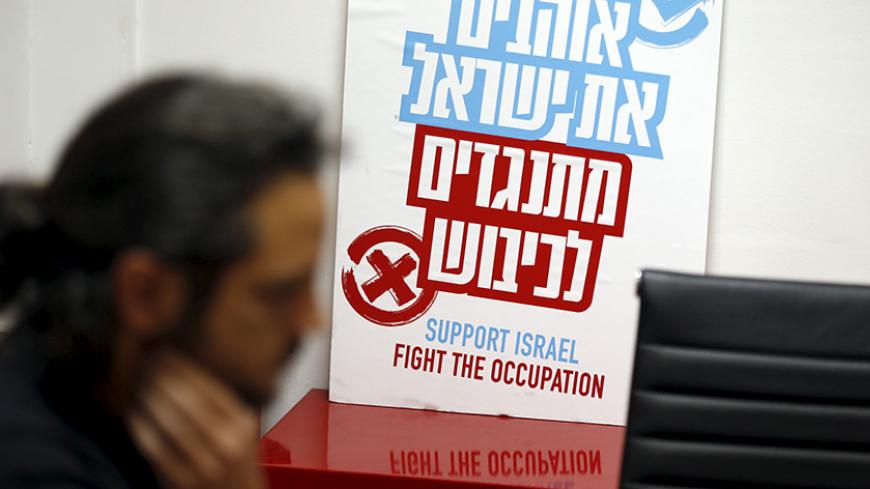 An employee of Peace Now, an Israeli NGO that tracks and opposes Jewish settlement in the occupied West Bank and East Jerusalem, works near a placard at their offices in Tel Aviv January 31, 2016. The placard in Hebrew reads, "Love Israel. Against the occupation". Picture taken January 31, 2016. REUTERS/Baz Ratner - RTX25Z92