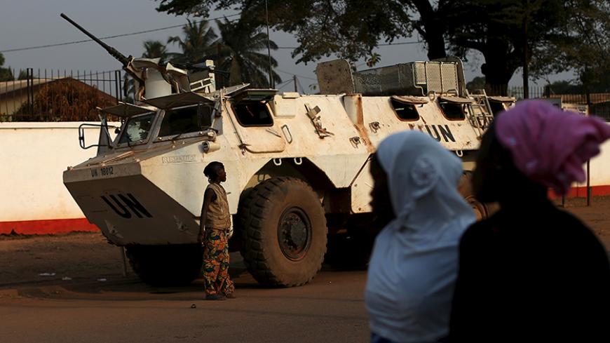 Women walk by a United Nations peacekeeping armoured vehicle guarding the outer perimeter of a compound of a school used as an electoral centre at the end of the presidential and legislative elections, in the mostly muslim PK5 neighbourhood of Bangui, Central African Republic, February 14, 2016. REUTERS/Siegfried Modola  - RTX26WL3