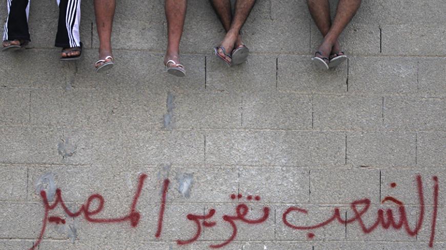 Shi'ite Bahraini men sit on a wall with graffiti that reads ''People want self-determination", as they attend a rally held by the Wefaq opposition party, in the village of Boori, south of Manama, October 14, 2011, to mark the 8-month anniversary of the February 14 uprising. REUTERS/Hamad I Mohammed (BAHRAIN - Tags: CIVIL UNREST POLITICS) - RTR2SO9O