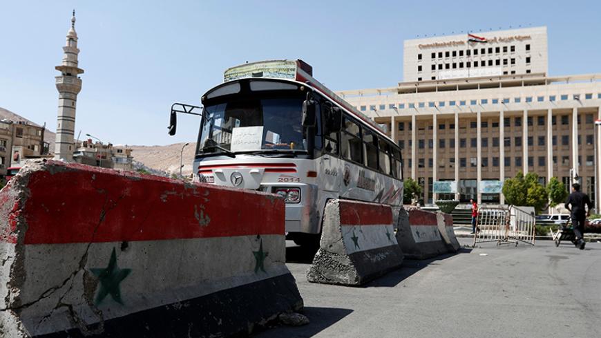 A bus drives past concrete blocks painted with the Syrian flag near the Central Bank of Syria in Damascus, Syria May 31, 2016. REUTERS/Omar Sanadiki - RTX2EZEA