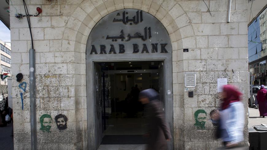 Palestinians walk past a bank in the West Bank city of Ramallah March 25, 2015. Israel's decision to withhold $130 million a month in revenue collected on behalf of the Palestinians is strangling the economy and leaving the banking system dangerously exposed, the Palestinian central bank governor said on Wednesday. REUTERS/Mohamad Torokman  - RTR4UT8C