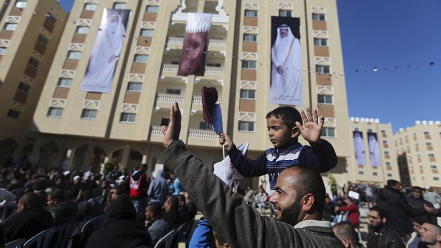 Posters depicting Qatar's former Emir Sheikh Hamad bin Khalifa al-Thani (R) and Emir of Qatar Tamim bin Hamad al-Thani (L) are seen on a building as a Palestinian man holding his son waves during the opening ceremony of Qatari-funded construction project "Hamad City", in Khan Younis in the southern Gaza Strip January 16, 2016. REUTERS/Ibraheem Abu Mustafa  - RTX22NS9