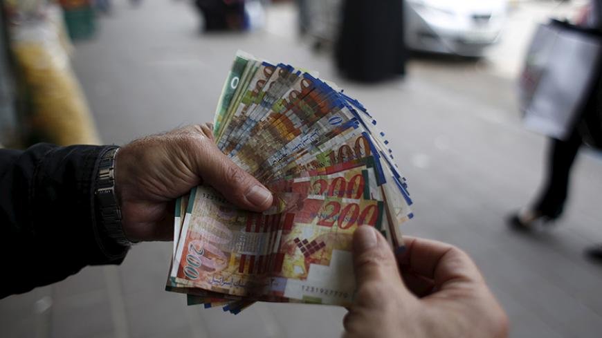 A Palestinian money exchanger displays money at a market in the West Bank city of Ramallah March 25, 2015. Israel's decision to withhold $130 million a month in revenue collected on behalf of the Palestinians is strangling the economy and leaving the banking system dangerously exposed, the Palestinian central bank governor said on Wednesday. REUTERS/Mohamad Torokman - RTR4UT7Y