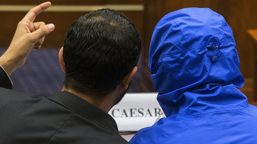 The man credited with smuggling 50,000 photos said to document Syrian government atrocities, a Syrian Army defector known by the protective alias Caesar (disguised in a hooded blue jacket), listens to his interpreter as he prepares to speak at a briefing to the House Foreign Affairs Committee on Capitol Hill in Washington July 31, 2014. REUTERS/Jonathan Ernst (UNITED STATES - Tags: POLITICS MILITARY) - RTR40T3S