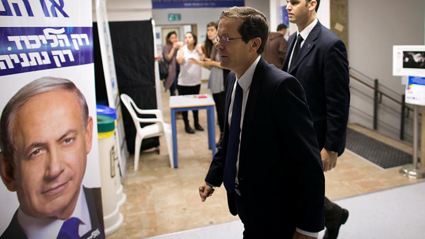 Isaac Herzog (C), co-leader of the Zionist Union party, walks past a Likud party campaign poster, that depicts Israeli Prime Minister Benjamin Netanyahu, as he arrives to address college students in Jerusalem March 10, 2015. REUTERS/Ronen Zvulun/File Photo - RTSEUAJ