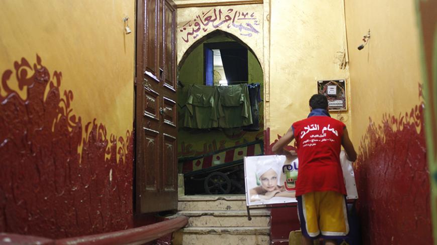 A worker holds a sign with a woman's image at the entrance of a traditional steam bath "hammam" in Cairo, September 15, 2014. The "hammam", which was adopted during Turkish rule, is similar to a sauna. Local steam bath culture was recently revived in past years after they were made cleaner, with modern methods of beauty and relaxation introduced. Picture taken September 15, 2014. REUTERS/Asmaa Waguih ? (EGYPT - Tags: SOCIETY) - RTR46MNO