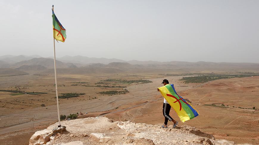An activist carrying a Berber flag walks on a hilltop above a silver mine, where dozens of poor and unemployed young villagers have been holding a permanent sit-in since 2011, near the town of Imider, southeastern Morocco, August 31, 2015. They have cut off the flow of water from a well that supplies one of the biggest silver mines in Africa. Protesters want to make the company hire more locals and reconsider its water and environmental policies. Picture taken August 31, 2015. REUTERS/Youssef Boudlal - RTX1