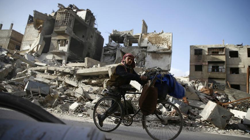 A handicapped man rides a bicycle past damaged buildings in the besieged town of Douma in eastern Ghouta in Damascus, Syria, March 1, 2018. REUTERS/Bassam Khabieh - RC19231603F0