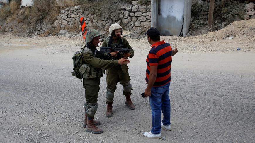 A Palestinian man stands in front of Israeli soldiers near the scene of attempted car ramming attack, in Hebron in the occupied West Bank June 2, 2018. REUTERS/Mussa Qawasma - RC1F06CFB530