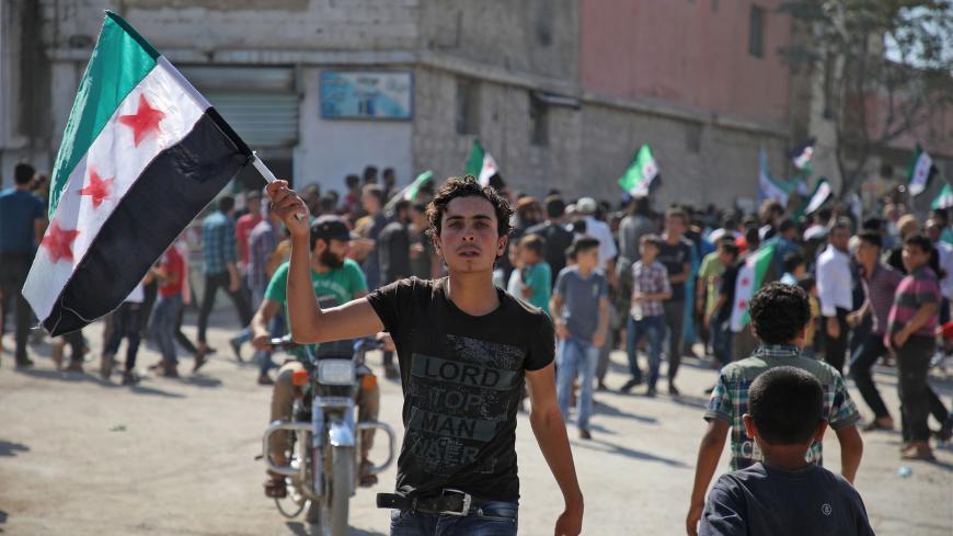 A Syrian youth waves an opposition flag during a demonstration against the Syrian government in the rebel-held town of Hazzanu, about 20 kilometres northwest of the city of Idlib, on September 21, 2018. (Photo by Aaref WATAD / AFP)        (Photo credit should read AAREF WATAD/AFP/Getty Images)