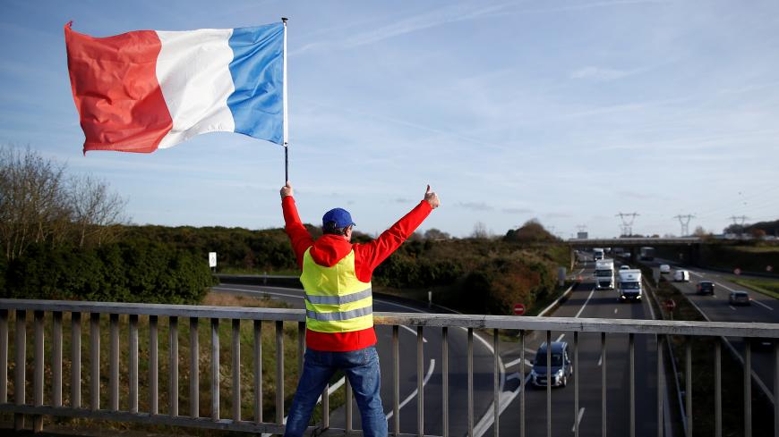 A man wearing a yellow vest and holding a French flag stands on a bridge near the Nantes Atlantique Airport as the "yellow vests" movement continues, in Bouguenais, France, December 11, 2018. REUTERS/Stephane Mahe - RC1FB4AA8210