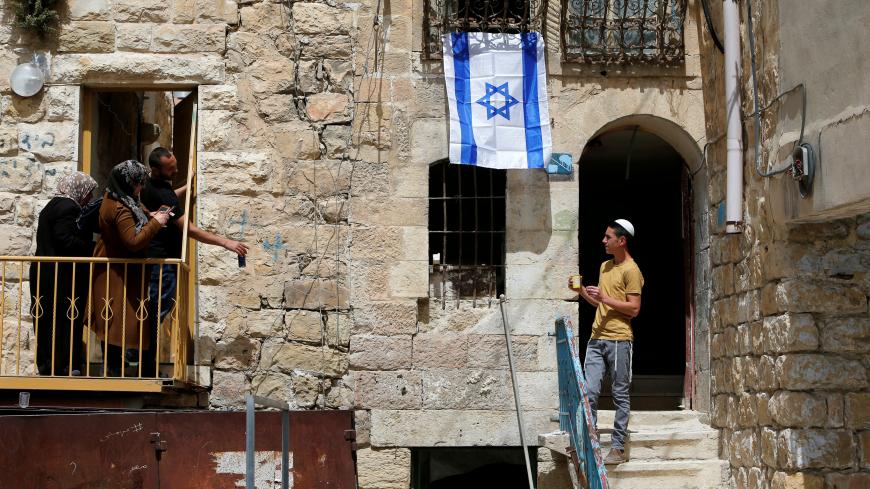 An Israel flag is seen hanging on a house as an Israeli settler looks at Palestinians in Hebron, in the occupied West Bank March 27, 2018. REUTERS/Mussa Qawasma     TPX IMAGES OF THE DAY - RC13D45CEAE0