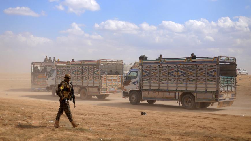 A fighter from the Syrian Democratic Forces (SDF) walks in front of two trucks, near the village of Baghouz, Deir Al Zor province, in Syria March 7, 2019. Picture taken March 7, 2019. REUTERS/Rodi Said - RC1438AC4EF0