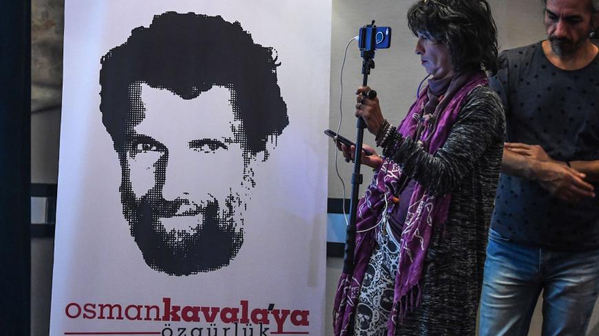 A journalist stands in front of a poster featuring jailed businessman and philanthropist Osman Kavala during a press conference of his lawyers on October 31, 2018. - Osman Kavala was arrested a year ago by Turkish authorities and has still to be charged with an offence. (Photo by OZAN KOSE / AFP)        (Photo credit should read OZAN KOSE/AFP via Getty Images)