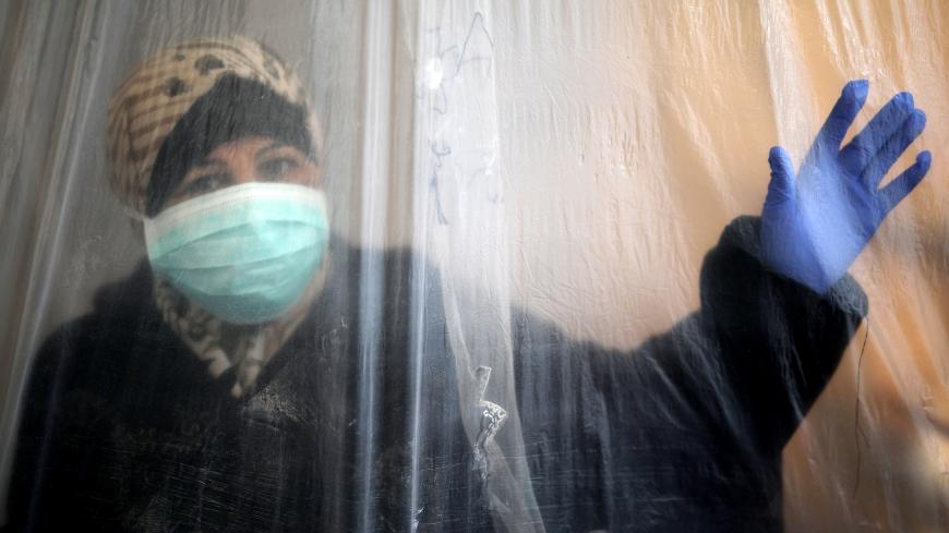A woman wearing a protective mask and  glove looks out through a nylon sheet covering part of she house in Beit Lahiya, northern Gaza Strip during the novel coronavirus pandemic crisis,on 11 April 2020.  (Photo by Majdi Fathi/NurPhoto via Getty Images)