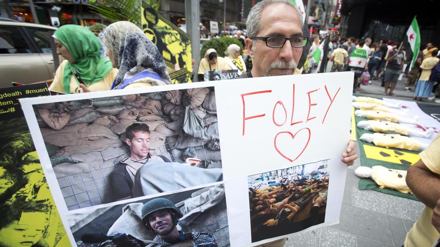 A man holds up a sign in memory of U.S. journalist James Foley during a protest against the Assad regime in Syria in Times Square in New York August 22, 2014. Foley, who was abducted in Syria in late 2012, was beheaded by a masked member of the Islamic State group in an act filmed in a video released on August 19 that also threatened a second American journalist, Steven Sotloff.   REUTERS/Carlo Allegri (UNITED STATES - Tags: SOCIETY CIVIL UNREST) - GM1EA8N0MAY01