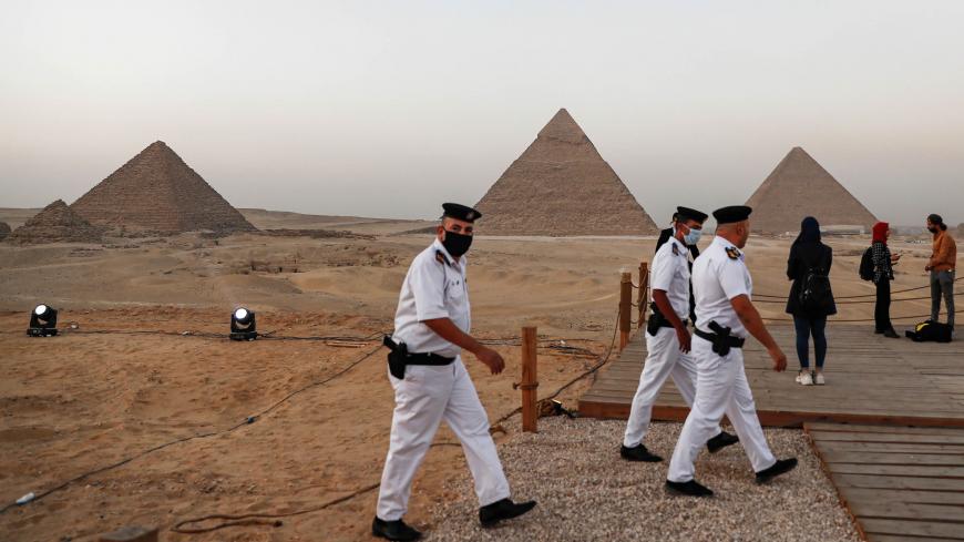 Policemen walk along a promontory overlooking (R to L) the Great Pyramid of Khufu (Cheops), the Pyramid of Khafre (Chephren), and the Pyramid of Menkaure (Menkheres) at the Giza Pyramids necropolis on the southwestern outskirts of the Egyptian capital Cairo on October 20, 2020 before an official ceremony launching the trial operations of the site's first environmentally-friendly electric bus and restaurant as part of a wider development plan at the necropolis. (Photo by Khaled DESOUKI / AFP) (Photo by KHALE