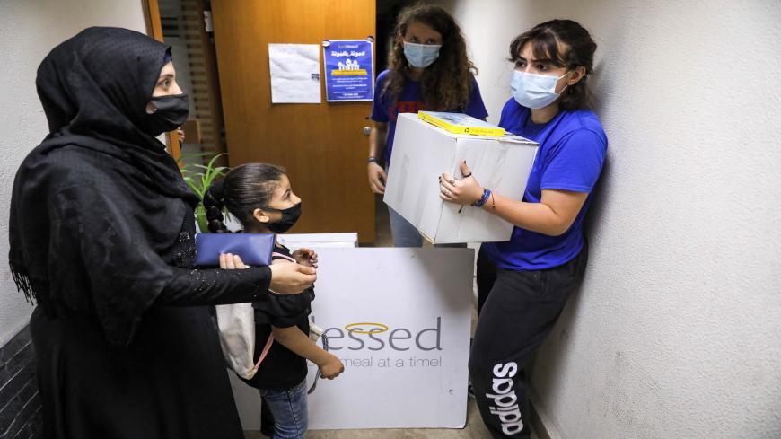 People arrive to receive food aid packages from workers, mask-clad due to the COVID-19 coronavirus pandemic, at the Food Blessed NGO's centre in Lebanon's capital Beirut on July 28, 2020. - Amid Lebanon's worst economic crisis since the 1975-1990 civil war, food aid has become a lifeline even for the once relatively affluent middle class. Lebanon's economy has collapsed in recent months, with the local currency plummeting against the dollar, businesses closing en masse and poverty soaring at the same alarmi