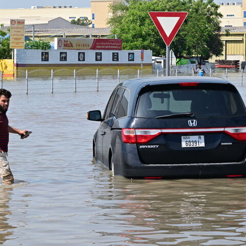 A man walks past a stranded car on a flooded street in Dubai following heavy rains on April 18, 2024. 
