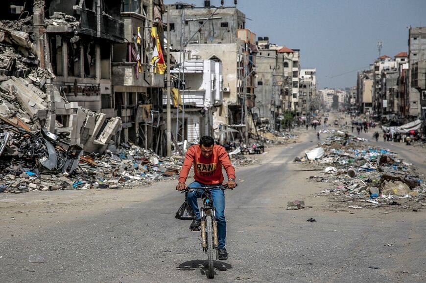 A man rides a bicycle past destroyed buildings along a street in Gaza City on March 27, 2024