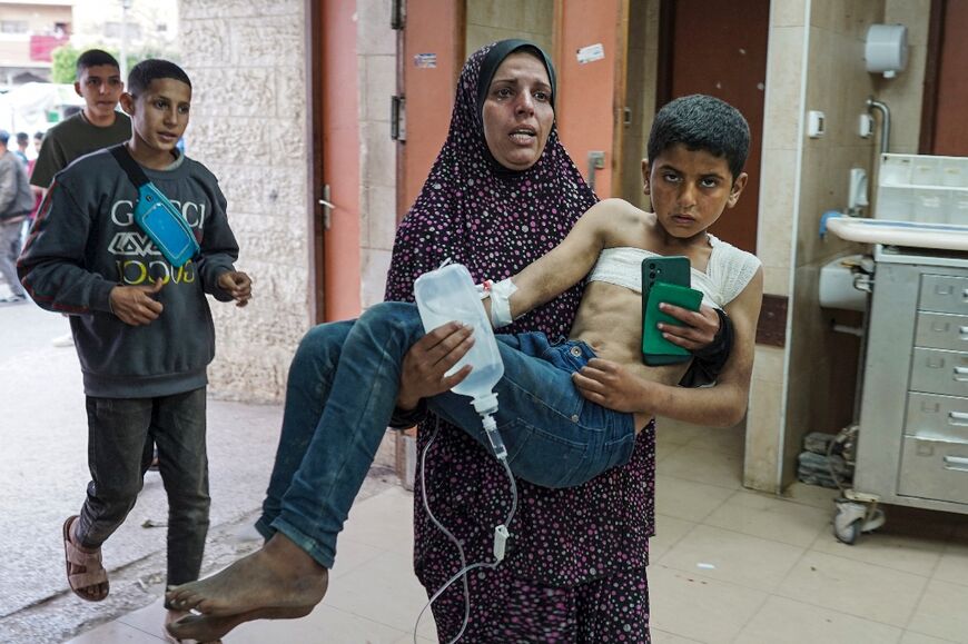 A Palestinian woman carries an injured child into a hospital as the Israel-Hamas war grinds on