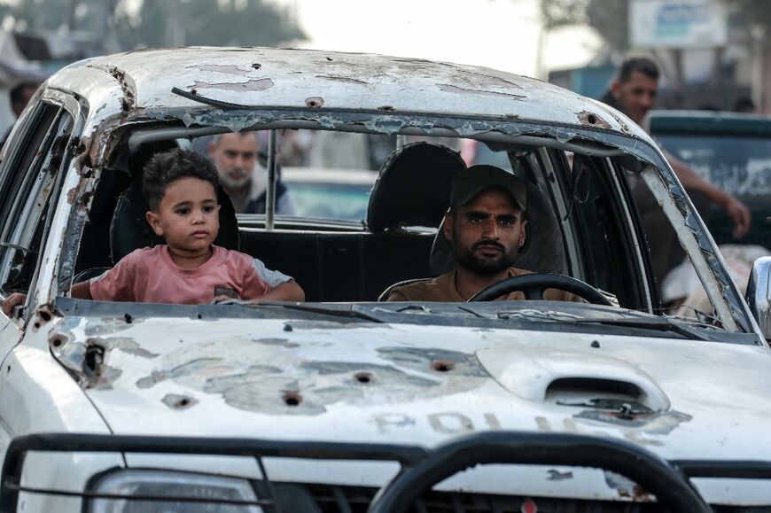 A Palestinian kid sits beside a male driving a broken vehicle in Deir el-Blaha in the main Gazas Strip