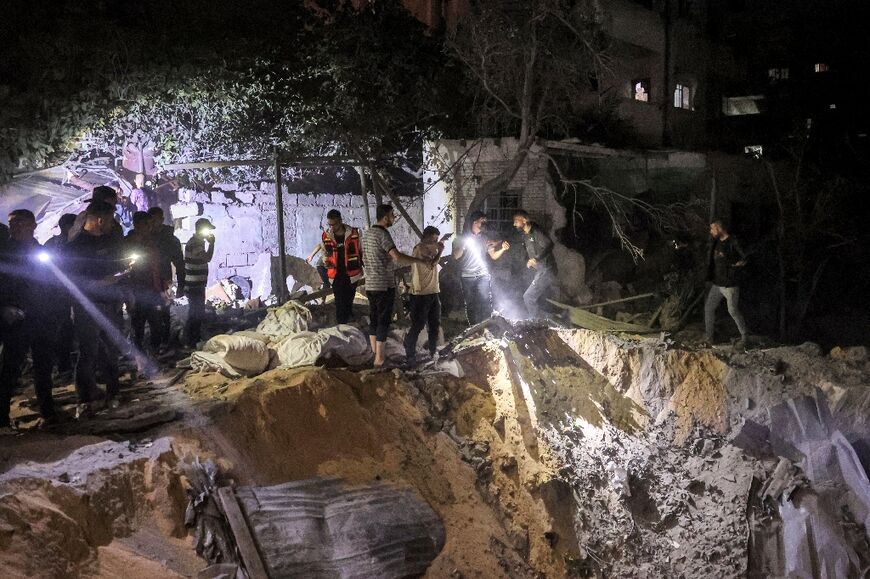 People search with flashlights by an impact crater at the site of a building that was hit by Israeli bombardment in Rafah in the southern Gaza Strip 