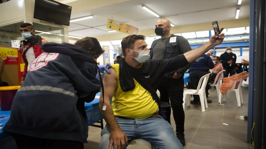A Palestinian man who works in Israel takes a selfie as he receives the first dose of a Moderna COVID-19 vaccine by an Israeli medical worker at the Meitar crossing checkpoint between the West bank and Israel, March 9, 2021. 