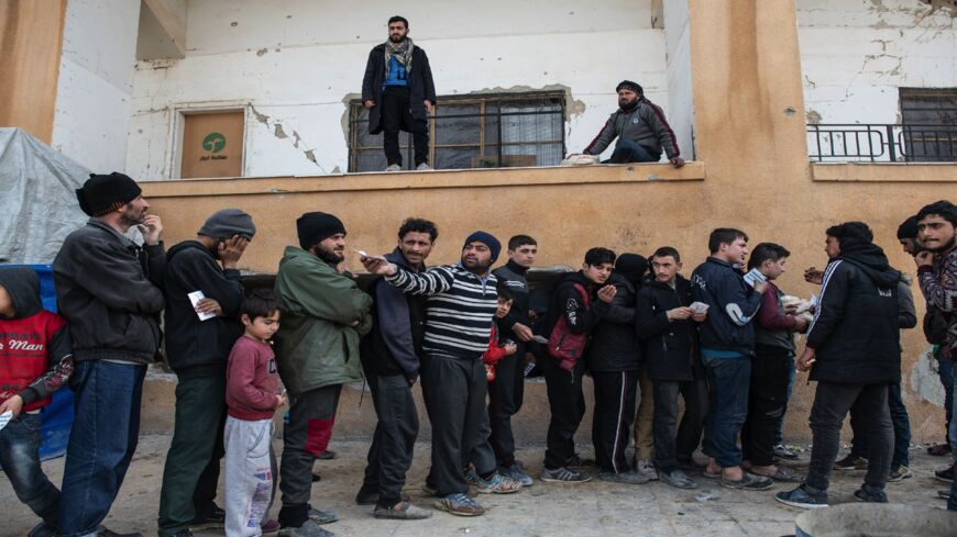 Displaced Syrians wait in a queue as an NGO delivers bread as they wait to receive humanitarian aid in a stadium that has been turned into a makeshift refugee shelter on Feb. 19, 2020, in Idlib, Syria. 