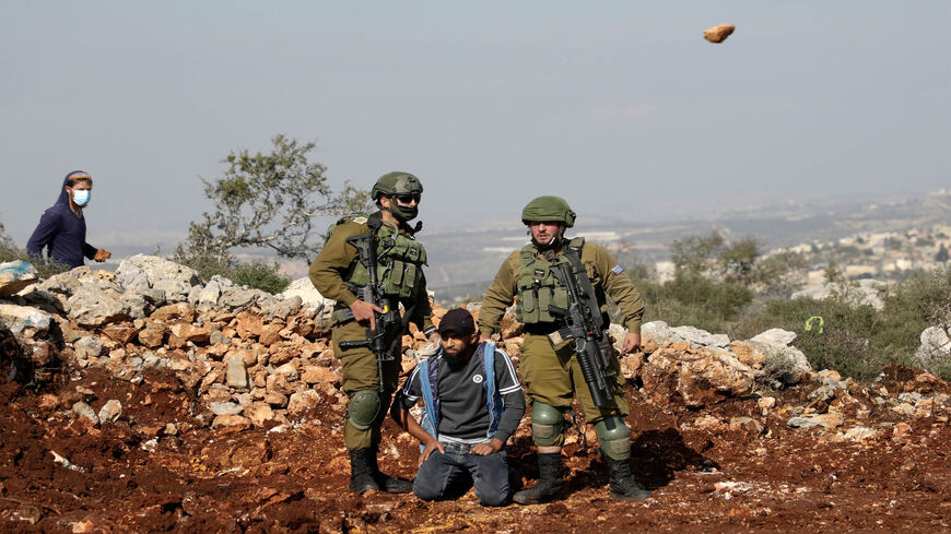 Israeli soldiers detain a Palestinian protester as an Israeli settler hurls rocks at Palestinians during a demonstration against the expansion of settlements in the town of Salfit, near the Israeli settlement of Ariel, West Bank, Nov. 30, 2020.