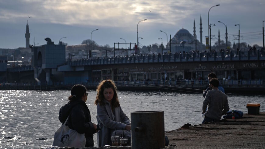 People sit along the Bosphorus shore at Karakoy port in Istanbul on Feb. 8, 2021 as the Galata bridge and the Suleymaniye mosque are seen in the background. 