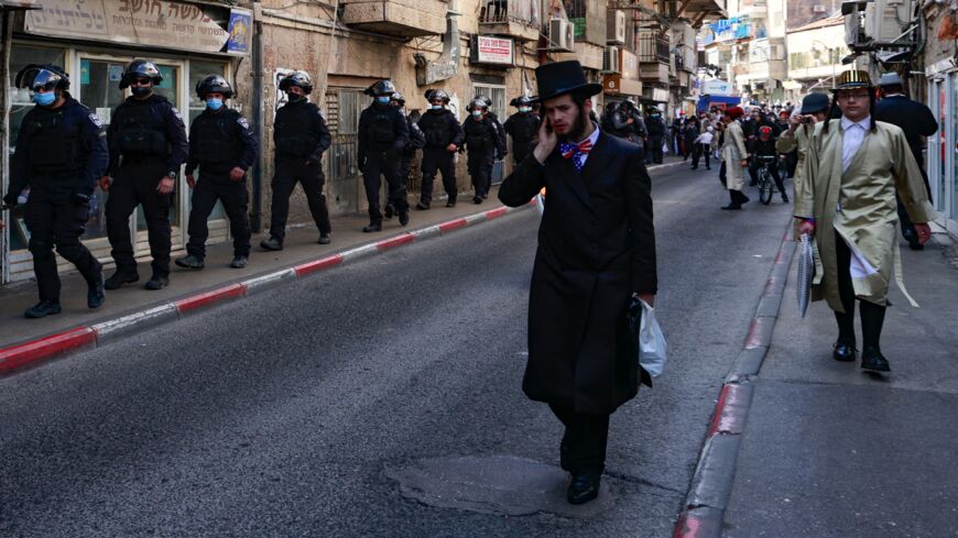 Orthodox Jewish men, some dressed in costumes to celebrate Purim, watch as Israeli policemen patrol in the neighborhood of Mea Shearim in Jerusalem, on Feb. 28, 2021.