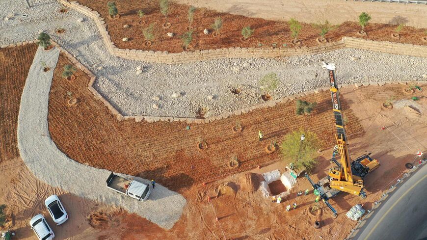 An aerial picture shows workers using a crane to plant trees in a park project by the roadside in the Saudi capital Riyadh, on March 29, 2021.
