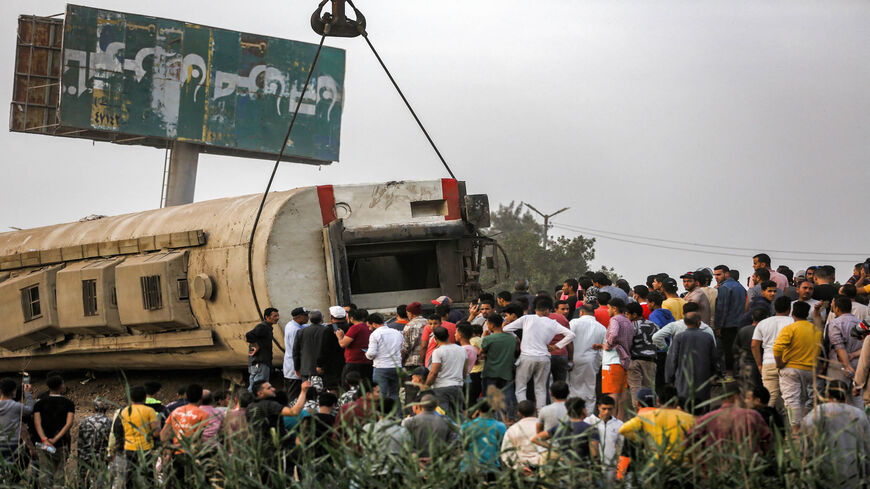 People watch as a telescopic railway crane lifts an overturned passenger carriage at the scene of a railway accident in the city of Toukh, central Nile Delta province of Qalyubiya, Egypt, April 18, 2021.
