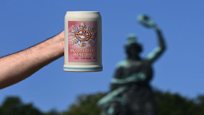 A man holds up the official 2020 Oktoberfest beer mug in front of the Bavaria monument at Theresienwiese in Munich, southern Germany, the place of the yearly beer festival, on Sept. 19, 2020. The traditional Bavarian Oktoberfest beer festival would have started today, but it was canceled a few months ago due to the ongoing novel coronavirus COVID-19 pandemic.