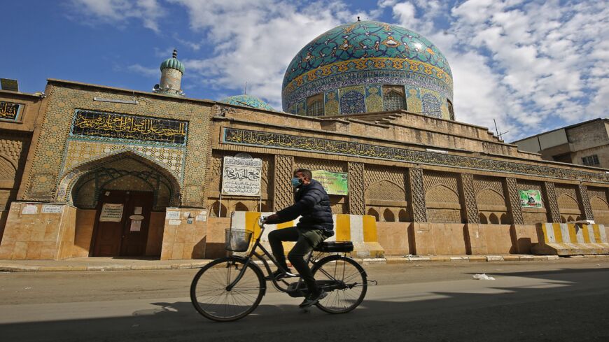 An Iraqi man rides his bicycle past a closed mosque in Baghdad on Feb. 19, 2021, as authorities reimposed partial lockdown measures until early March after detecting a new strain of the coronavirus. 