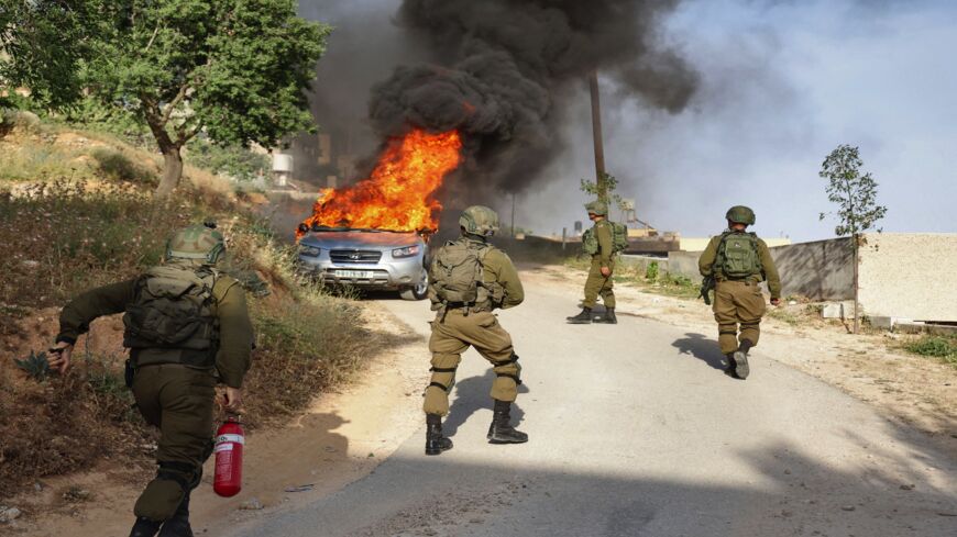 An Israeli soldier tries to extinguish flames in a burning Palestinian vehicle during a security operation in the village of Aqraba, east of Nablus in the occupied West Bank, on May 3, 2021. The vehicle is suspected to have been used in a drive-by shooting of Israelis the previous day at a bus station at Tapuah junction south of Nablus.