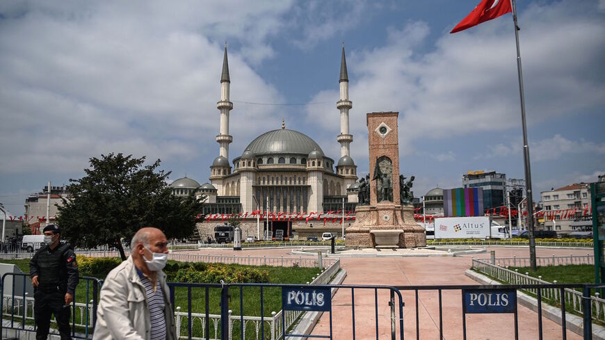 A man passes by a Turkish anti riot police officer stands guard during the Friday prayers during the inauguration of a 4000-capacity mosque in Istanbul's iconic Taksim square on May 28, 2021. 