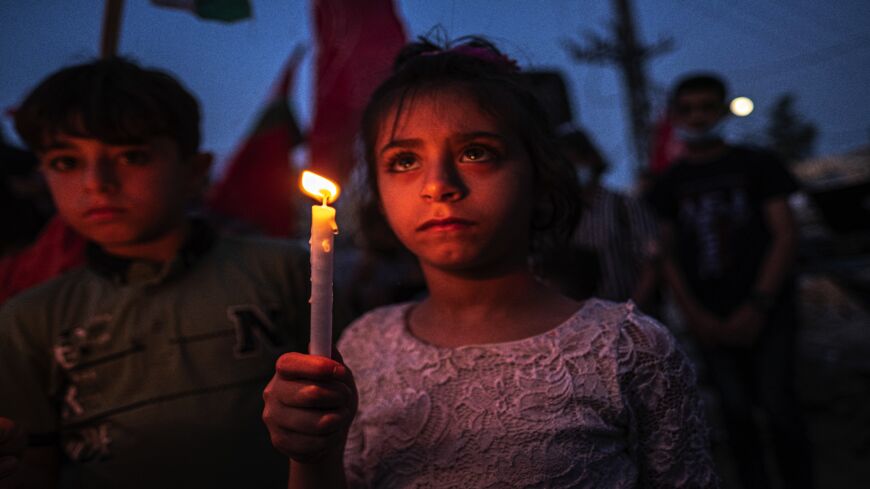 Palestinian children hold candles during a rally amid the ruins of houses allegedly destroyed by Israeli strikes, in Beit Lahia, northern Gaza Strip, on May 25, 2021, in Gaza City, Gaza.