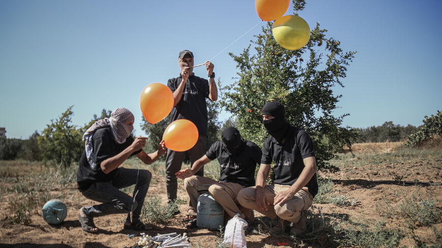 Masked Palestinian supporters of the Al-Nasir Salah Al-Din Brigades prepare incendiary balloons to launch across the border fence east of Gaza city towards Israel, on June 16, 2021 east of Gaza City in Gaza. 