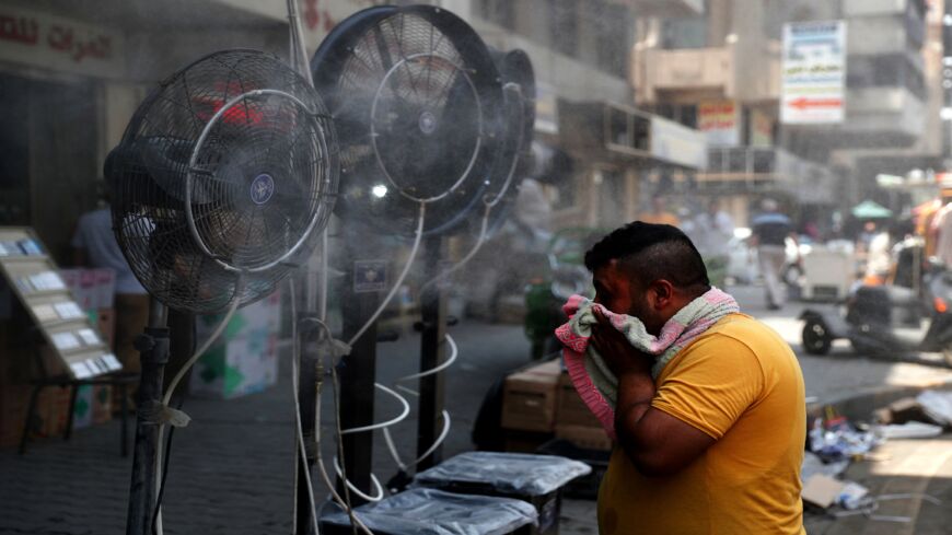 A man stands by fans spraying air mixed with water vapor deployed by donors to cool down pedestrians along a street in Iraq's capital, Baghdad, on June 30, 2021, amidst a severe heatwave. 