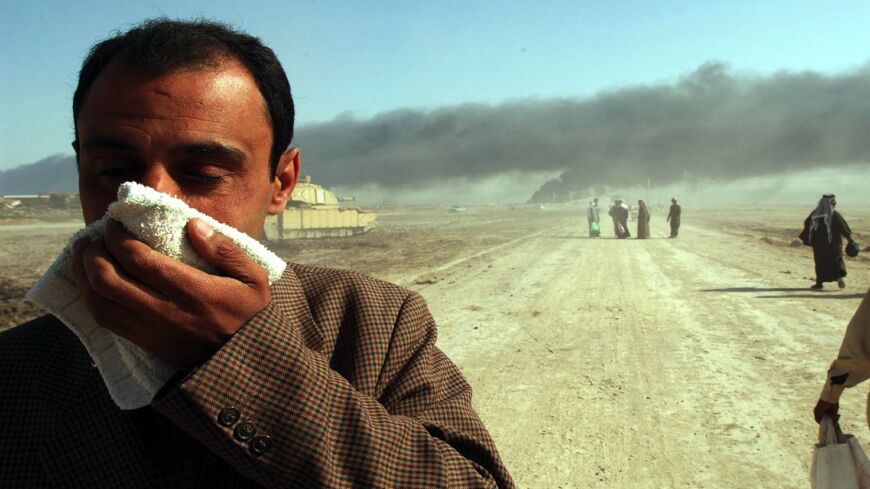 As oil fires burn in the distance, a man covers his face near the entrance to the besieged city of Basra on March 29, 2003, in Iraq. 