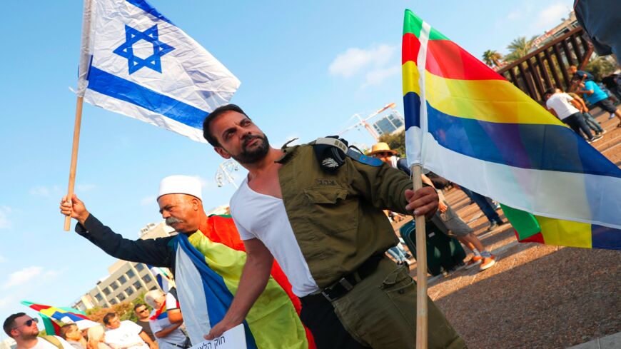 A former Israeli Druze officer (R) holds a banner that reads in Hebrew, "Bibi, look at the absurdity that you have created with your law,"