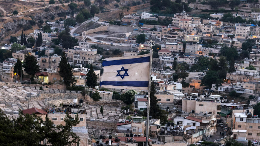 This picture taken from the Mount of the Olives shows an Israeli flag flying with the predominantly Arab neighborhood of Silwan in the background, Jerusalem, July 1, 2021.