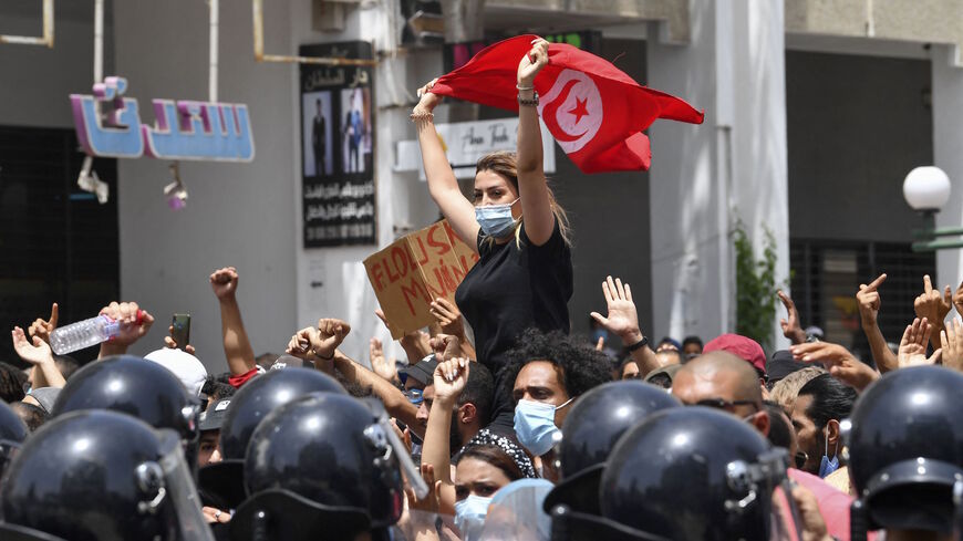 A Tunisian protester lifts a national flag at an anti-government rally as security forces block off the road in front of the Parliament in the capital Tunis on July 25, 2021. 