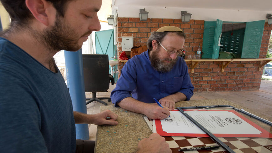Rabi Aaron Leibowitz (C), the founder of Hashgach Pratit — Hebrew for private supervision — which checks if restaurants abide by kosher practices, signs a certificate for the new bar Eitan Steinberg in the center of Jerusalem, June 8, 2016.