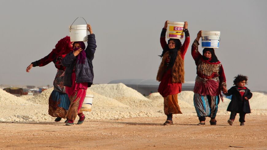 Syrian women whose families fled from shellings in the southern Idlib and Aleppo countryside carry buckets of water, January 22, 2018. 