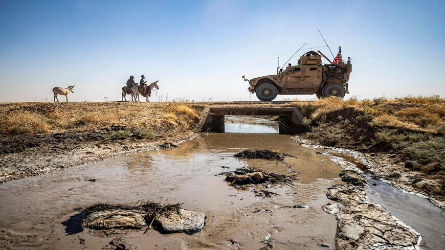 Youths ride donkeys near a US military vehicle crossing a stream polluted by an oil spill near the village of Sukayriyah, in the countryside south of Rumaylan (Rmeilan) in the Kurdish-controlled northeastern Hasakeh province, Syria, July 19, 2020.
