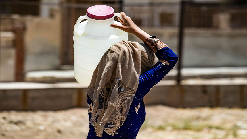 A Syrian woman carries a container of water provided by UNICEF in the northeastern city of Hasakah, after disruption in water supply from the Alouk station, Syria, July 8, 2021.